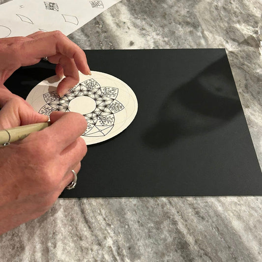 Person drawing a Zentangle mandala with a black pen on a round tile